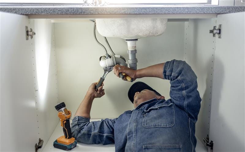 Plumber repairing pipes beneath a bathroom sink in Panama City Beach