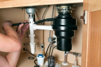 Plumber repairing a garbage disposal beneath a kitchen sink in Panama City Beach