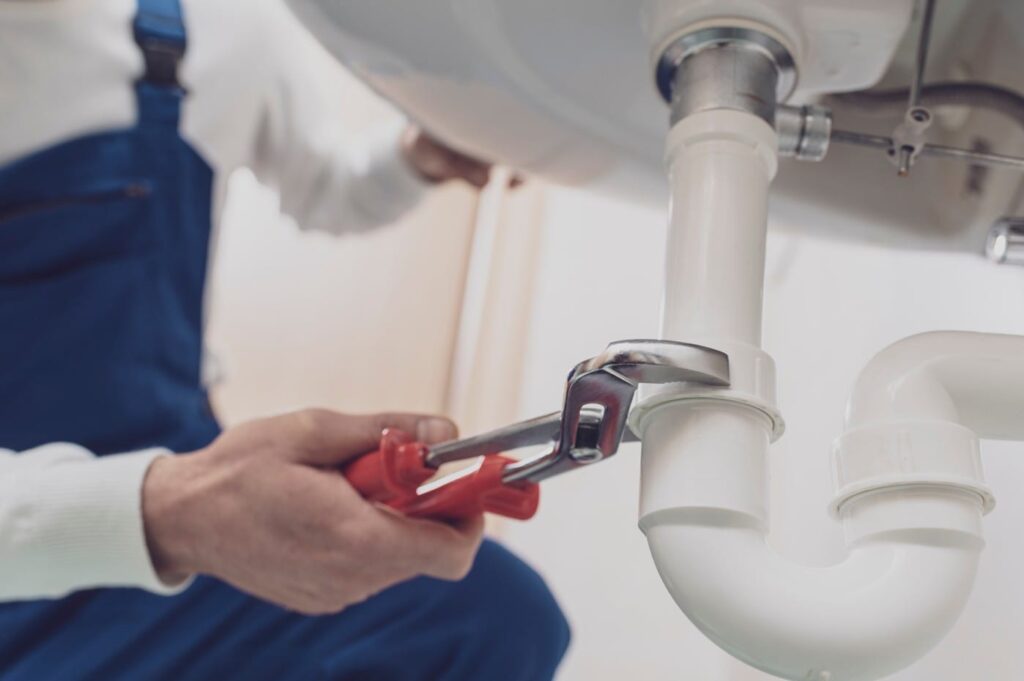 Plumber repairing a white drain pipe beneath a sink in Panama City Beach
