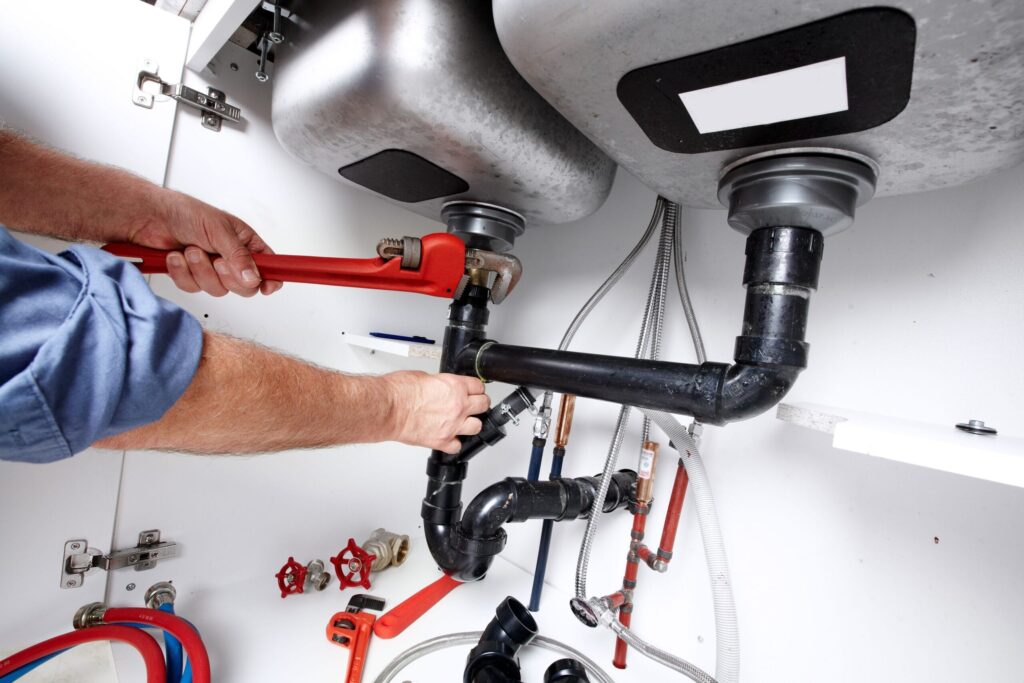 Plumber repairing drain pipes beneath a kitchen sink in Panama City Beach